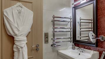 A bathroom with a white sink, chrome towel racks, a mirror, and a robe hanging on a door.
