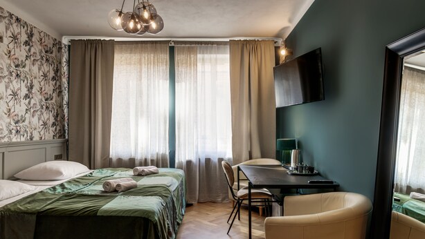 Habitación de hotel con cama, escritorio, silla, televisor y ventana con cortinas.