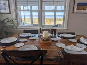 A dining table set for six with a view of the beach through large windows.