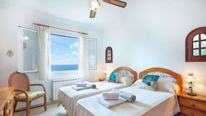 A hotel room with two beds, a view of the sea, a wooden ceiling fan, and a wooden dresser.