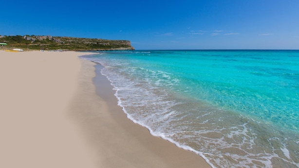 A beach with clear turquoise waters and a sandy shore.