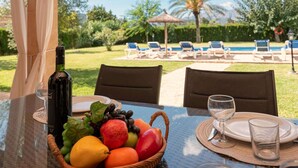 Ein Tisch mit einer Weinflasche, einem Obstkorb und Blick auf einen Poolbereich mit Liegestühlen und einer Palme.