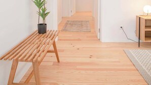 Ein Korridor mit Holzboden, einer Bank, einem Blumentopf, einem Spiegel, einer Wandleuchte und einem gerahmten Kunstwerk.