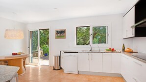 A modern kitchen with white cabinets, a granite countertop, and a view of greenery through the windows.
