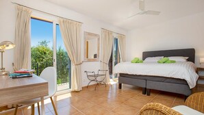 A bedroom with a bed, a desk, a chair, a balcony, and a ceiling fan.