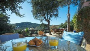 A table with croissants and orange juice, overlooking a scenic view with trees and a distant mountain.