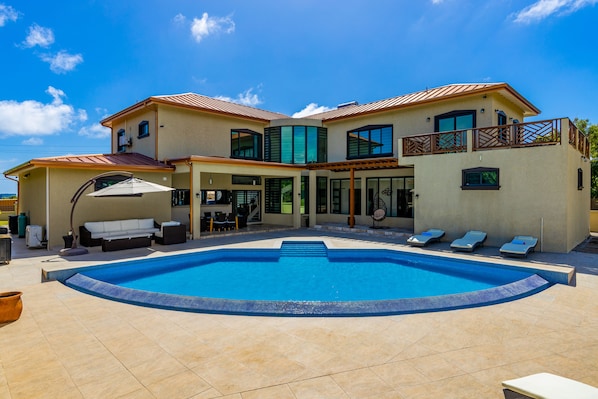 A two-story house with a swimming pool, outdoor seating, and a balcony.