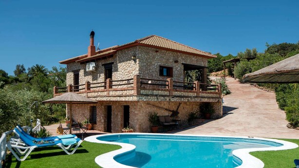 A stone house with a swimming pool, a patio with lounge chairs, and a staircase leading to a balcony.