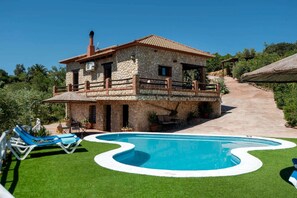 Une maison en pierre avec une piscine, un patio doté de chaises longues et un escalier menant à un balcon.