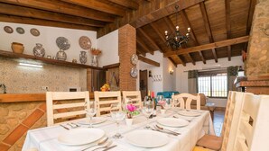 A dining area with a long table set for a meal, wooden chairs, and a brick wall with decorative plates. - Casa Irene - Four Bedroom Villa, Sleeps 7 (El Gastor)