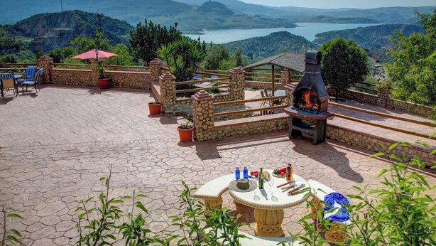 A patio with stone flooring, a round table with chairs, a stone fireplace, and a view of mountains and a lake. - Casa Irene - Four Bedroom Villa, Sleeps 7 (El Gastor)