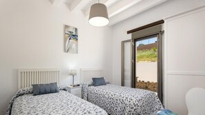 A bedroom with two beds, a nightstand, a chair, a window, and a ceiling light. - El Granadino - Two Bedroom Villa, Sleeps 4 (El Gastor)