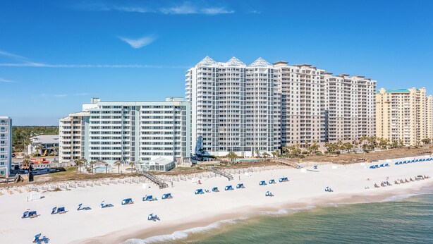 A beachfront hotel with multiple high-rise buildings, a sandy beach with blue umbrellas, and a clear blue sky. - The 9th Floor Offers A True Blue View Of The Sparkling Gulf Of Mexico! (pensacola)