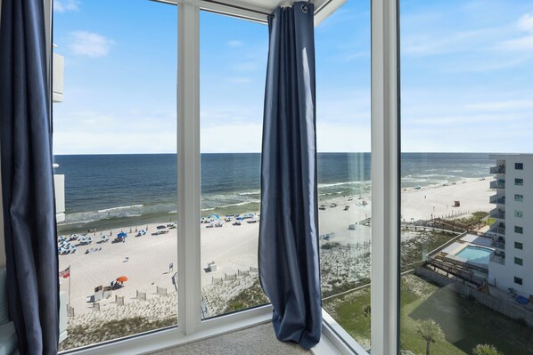 A view from a window overlooking a beach with umbrellas and a pool area.