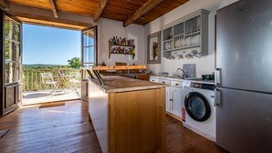 Una cucina con pavimento in legno, lavatrice integrata, frigorifero in acciaio inossidabile e un'ampia finestra con vista panoramica.
