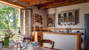 Cucina con travi in legno, tavolo da pranzo con servizio da tè e vista sul verde circostante.