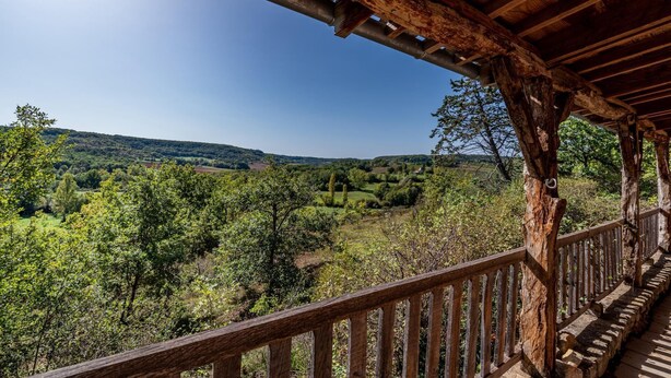 Un balcone in legno con vista su un paesaggio verdeggiante e dolci colline all'orizzonte.