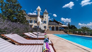 A poolside area with lounge chairs and a colorful towel, a large building with a tower in the background, and a clear blue sky.
