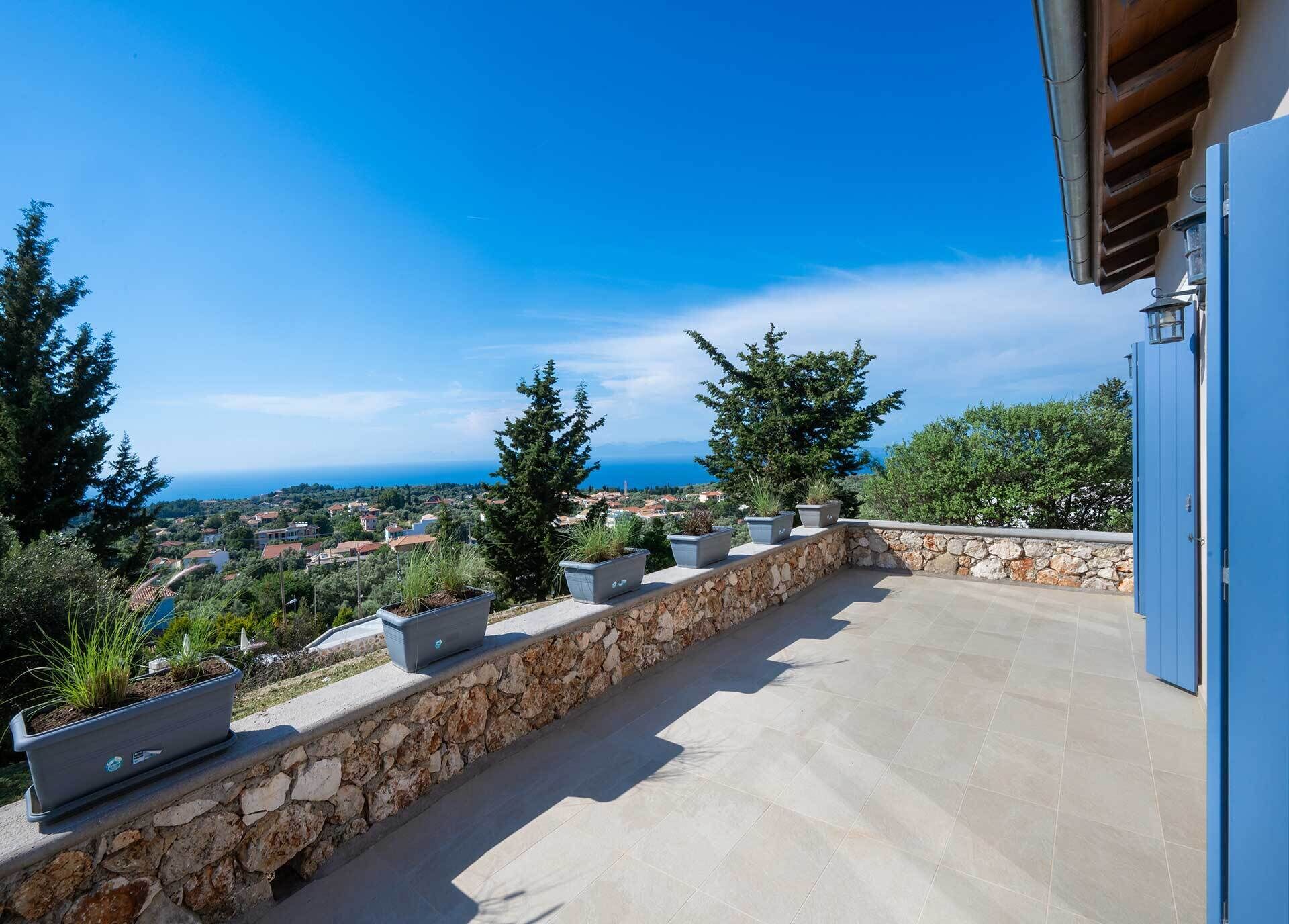 Una terraza con muros de piedra, plantas en macetas y vistas a un pueblo costero.