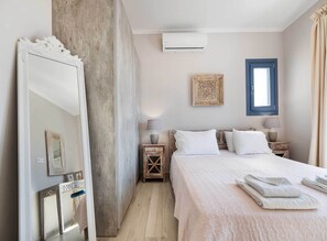 Ein Schlafzimmer mit einem Bett, Nachttischen, einem Spiegel, einem Fenster und einer Klimaanlage.