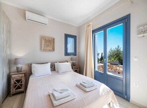 A bedroom with a large bed, a window, a wall-mounted air conditioner, and a decorative wall piece.