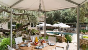 An outdoor dining area with a round table, white chairs, and umbrellas, overlooking a pool and garden. - Eratito - Three Bedroom Villa, Sleeps 6 (Tsoukalades)