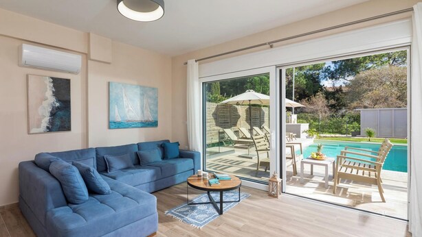 Een moderne woonkamer met een blauwe bank, een salontafel en uitzicht op een zwembad en tuinmeubilair.