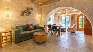A cozy interior with a stone wall, a green sofa, a round wicker table, and a wooden dining table with chairs.