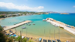 A coastal town with clear turquoise waters, a sandy beach, and a rocky breakwater.