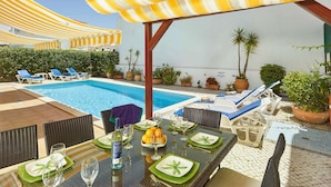Uma área à beira da piscina com espreguiçadeiras, uma mesa de jantar para dois e uma piscina.