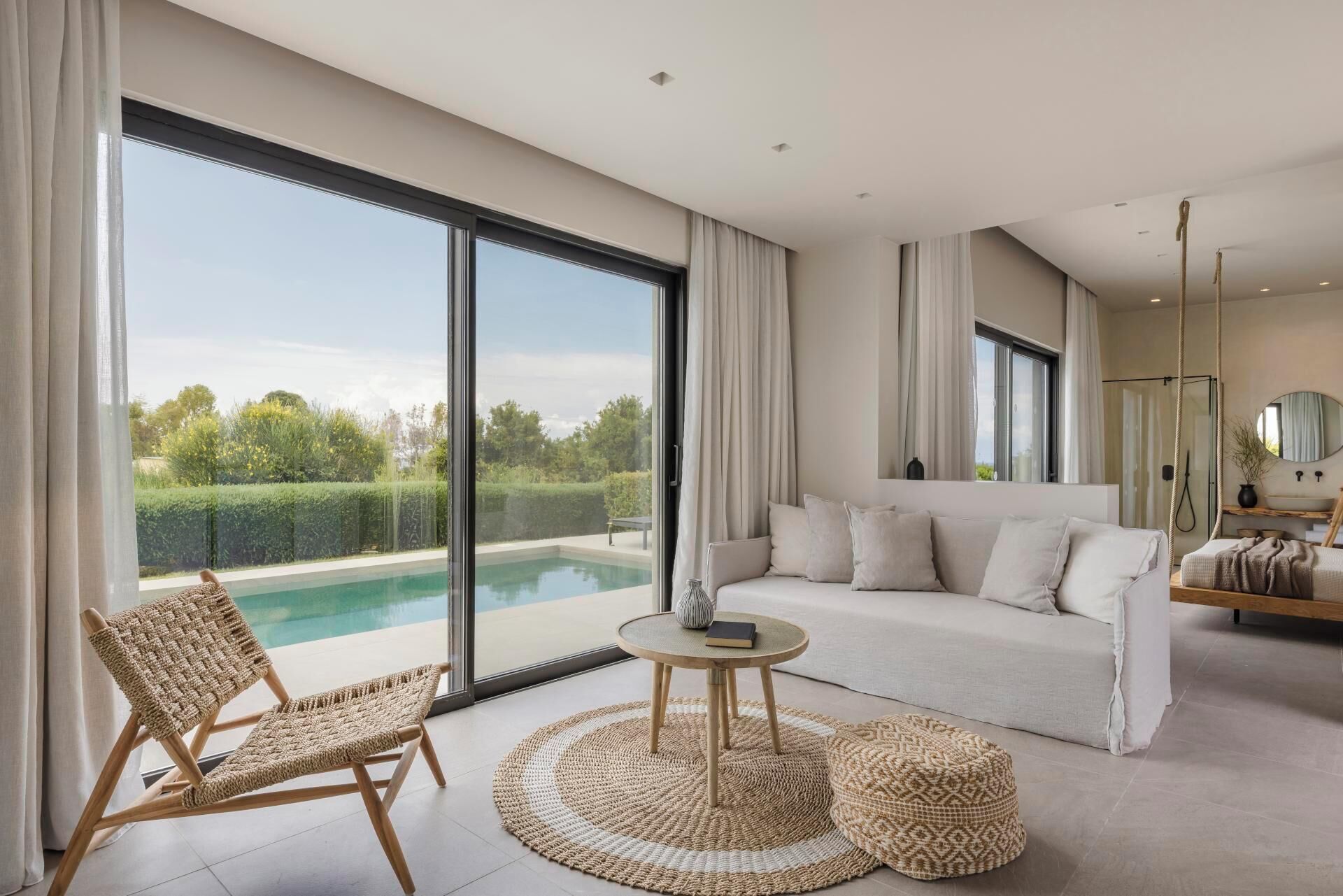 A modern living room with a large glass door leading to a pool, a sofa, a round table, and a chair.
