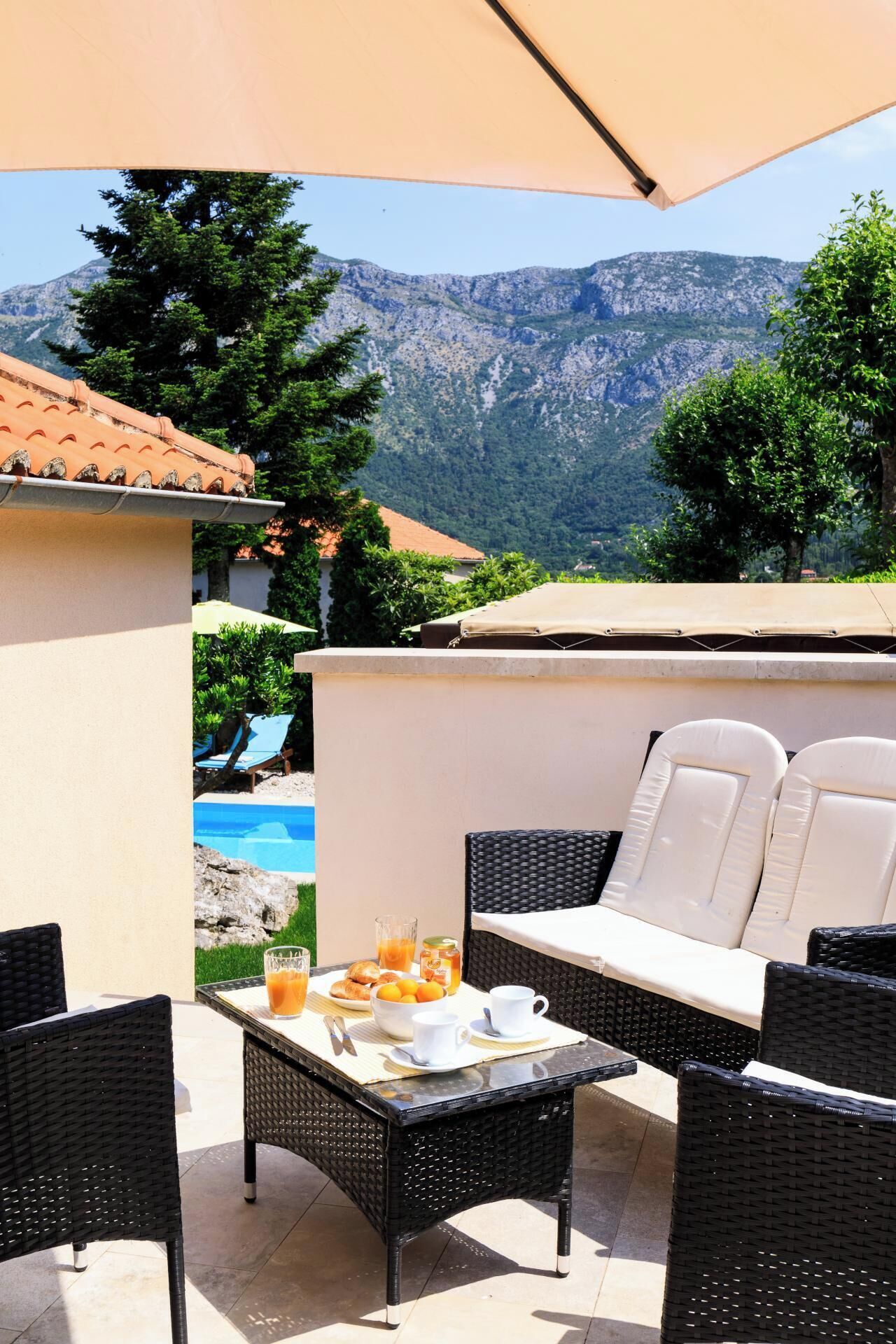 An outdoor patio with a table set for breakfast, wicker chairs, and a sofa with cushions.