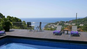 Un espace piscine avec vue sur la mer, comprenant deux chaises longues, une table et une plante en pot.