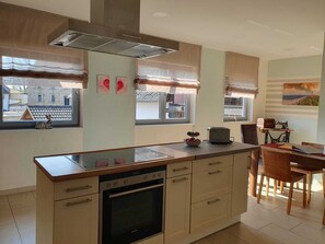 A modern kitchen with a central island, built-in oven, and a dining area with a table and chairs.