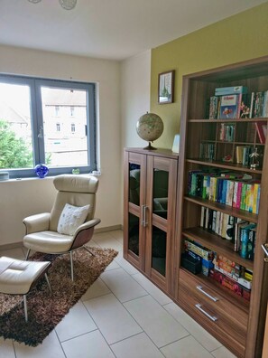 A room with a large window, a globe on a cabinet, a chair, and a bookshelf filled with books.