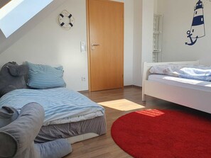 A bedroom with a loft bed, a smaller bed, a red rug, a wooden door, and a wall decoration of a lighthouse.
