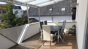 A covered outdoor patio with a table and chairs, a wooden deck, and a view of neighboring houses. - Relaxation oasis in the heart of Rheinhessen, Haus Weinbergsblick (Armsheim)