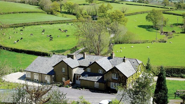 Een landhuis met een stenen gevel, omgeven door groene velden en grazende schapen.