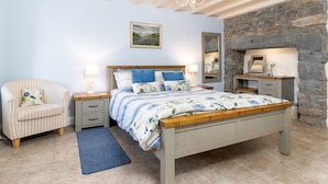 Een slaapkamer met een bed, nachtkastjes, een stoel, een vloerkleed, een schilderij en een stenen open haard.