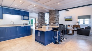 Een moderne keuken met blauwe kastjes, een centraal eiland met barkrukken en een stenen openhaard.