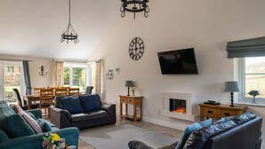Een woonkamer met een open haard, een televisie en een eethoek met een tafel en stoelen.
