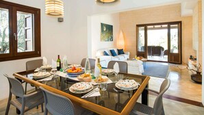 A dining area with a glass table, chairs, and a white sofa in the background. - Sa Rota Nova - Three Bedroom Villa, Sleeps 6 (Mallorca)