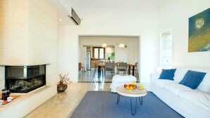 A modern living room with a fireplace, a dining area, and a sofa with blue cushions. - Sa Rota Nova - Three Bedroom Villa, Sleeps 6 (Mallorca)