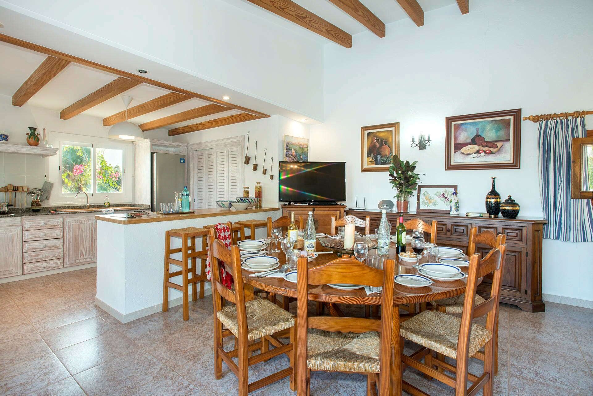 Un comedor amplio con una mesa y sillas de madera, una cocina al fondo y un televisor en la pared.