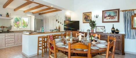 Un comedor amplio con una mesa y sillas de madera, una cocina al fondo y un televisor en la pared.