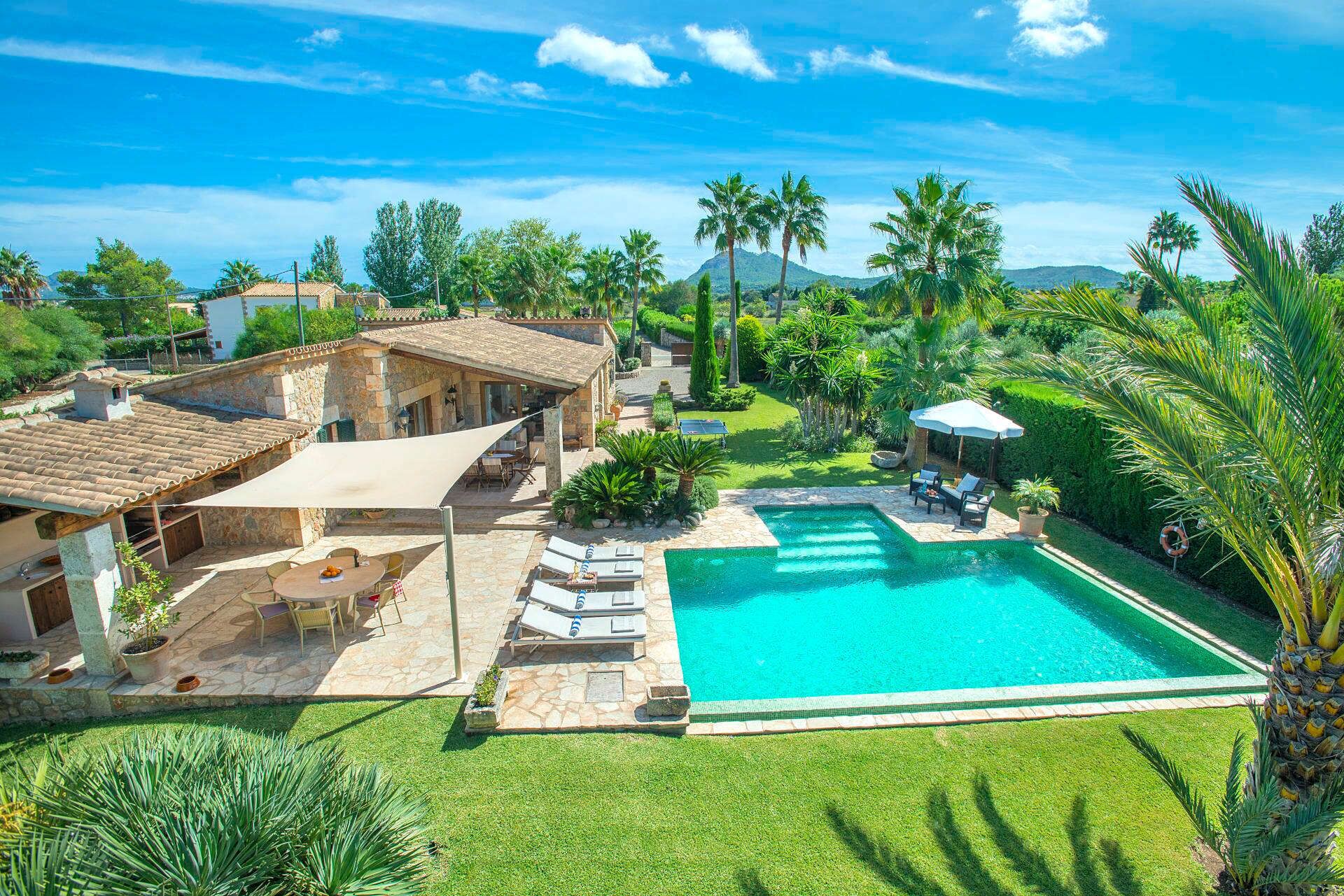 A large swimming pool with a stone deck, surrounded by lush greenery and palm trees.