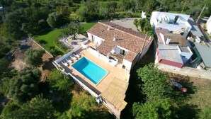Vue aérienne d’une propriété comprenant une piscine, un espace patio et une grande maison avec un toit en tuiles.