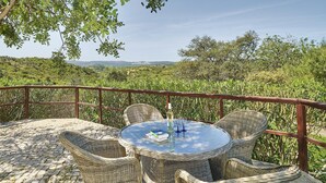 Un espace extérieur aménagé avec des chaises en osier et une table en verre, offrant une vue sur un paysage luxuriant.