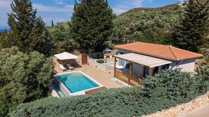 Una villa con piscina, un patio cubierto y un muro de piedra.