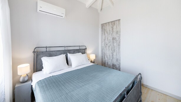 A bedroom with a bed, nightstands, a lamp, an air conditioning unit, and a rustic wall panel.